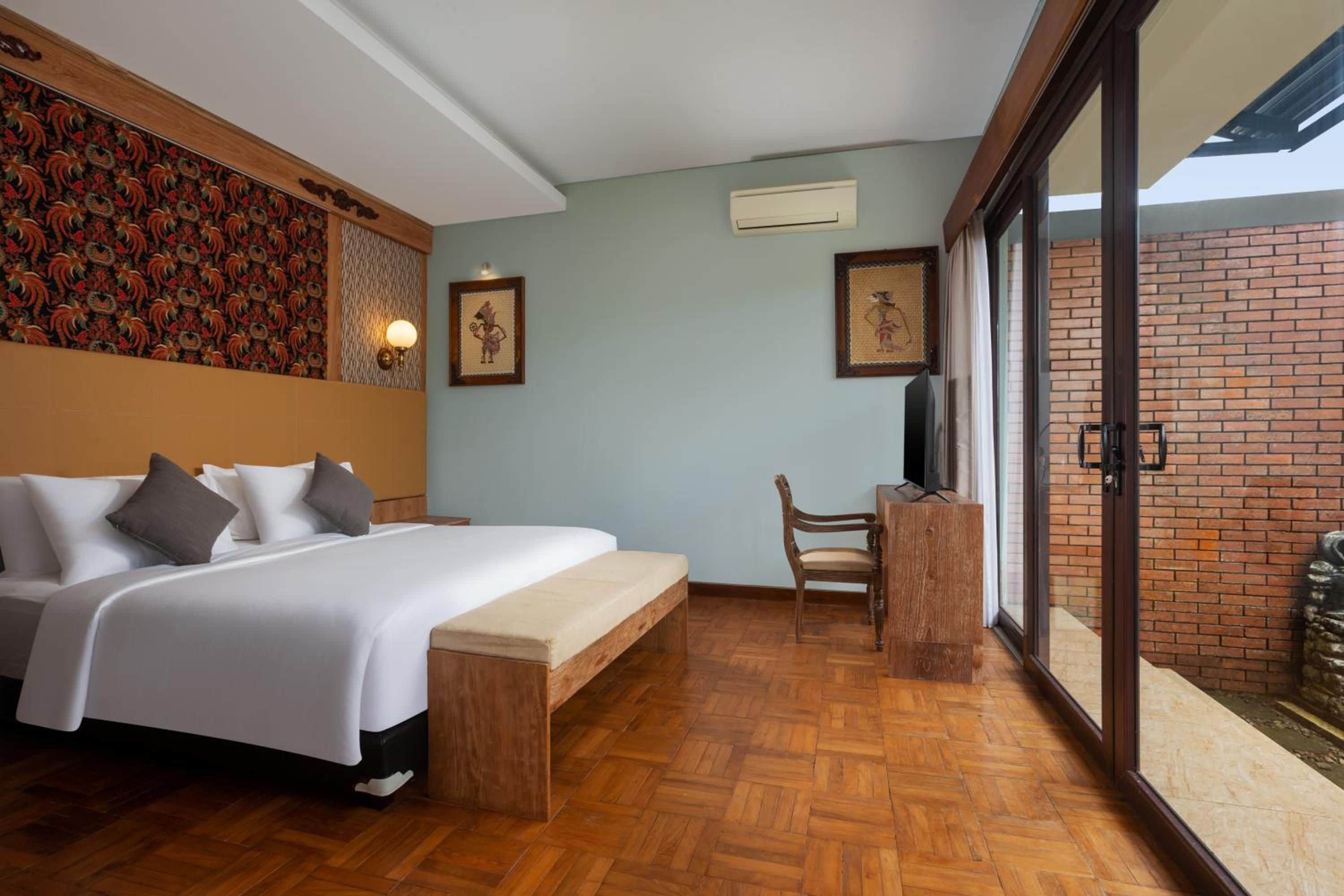 A hotel room with a bed, a desk, and a view of a brick wall.