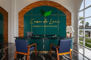 Mostrador de recepción con fondo verde, dos sillas azules y el logotipo de 'Casa de Lani Resort & Convention'.
