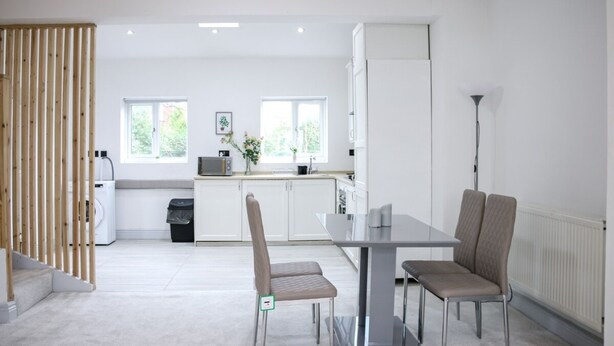 A modern kitchen with white cabinets, a dining table with chairs, and a view of the outdoors through large windows. - 3-bedroom House Bolton Town Centre Free Parking (Bolton)