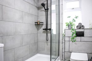 A modern bathroom with a glass shower enclosure, a white toilet, and a grey tiled wall. - 3-bedroom House Bolton Town Centre Free Parking (Bolton)