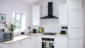 A kitchen with white cabinets, a black range hood, a microwave, a gas stove, and a sink. - 3-bedroom House Bolton Town Centre Free Parking (Bolton)