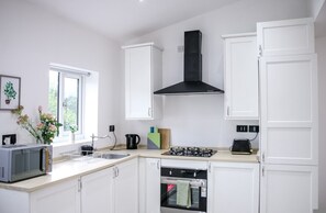 A kitchen with white cabinets, a black range hood, a microwave, a gas stove, and a sink. - 3-bedroom House Bolton Town Centre Free Parking (Bolton)
