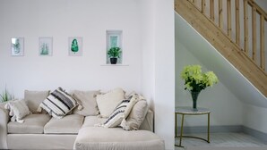 A living room with a beige sofa, a small table with a vase of flowers, a staircase, and wall-mounted plant art. - 3-bedroom House Bolton Town Centre Free Parking (Bolton)