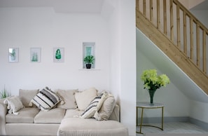 A living room with a beige sofa, a small table with a vase of flowers, a staircase, and wall-mounted plant art. - 3-bedroom House Bolton Town Centre Free Parking (Bolton)