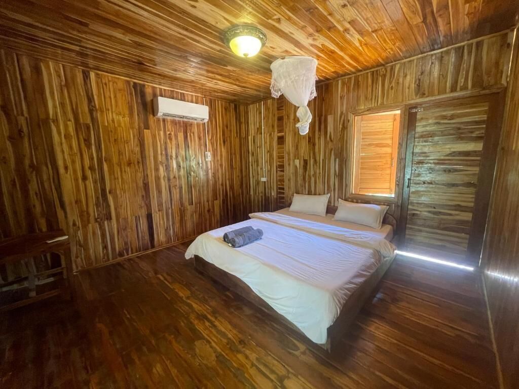 A wooden-paneled room with a bed, a hanging light fixture, and a window with blinds.