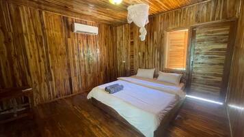 A wooden-paneled room with a bed, a hanging light fixture, and a window with blinds.