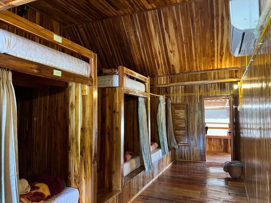 Una cabaña de madera con literas, piso de madera y una ventana pequeña.