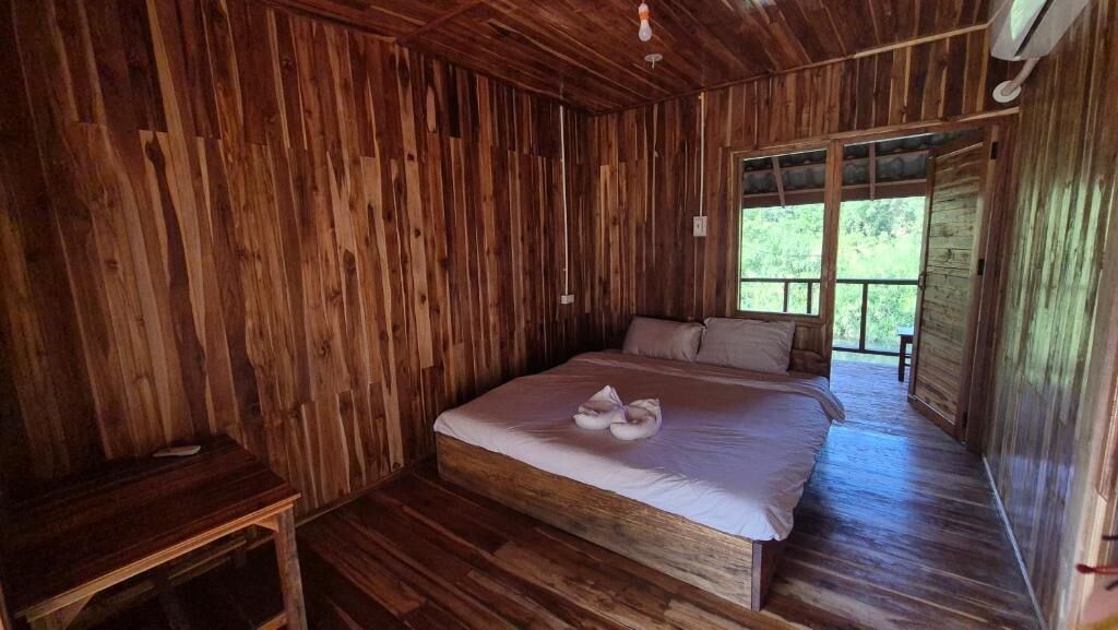 A wooden room with a bed, a small table, and a window.