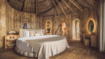 Una habitación con una cama grande, paredes de madera, un techo curvo y un tocador pequeño con espejo.