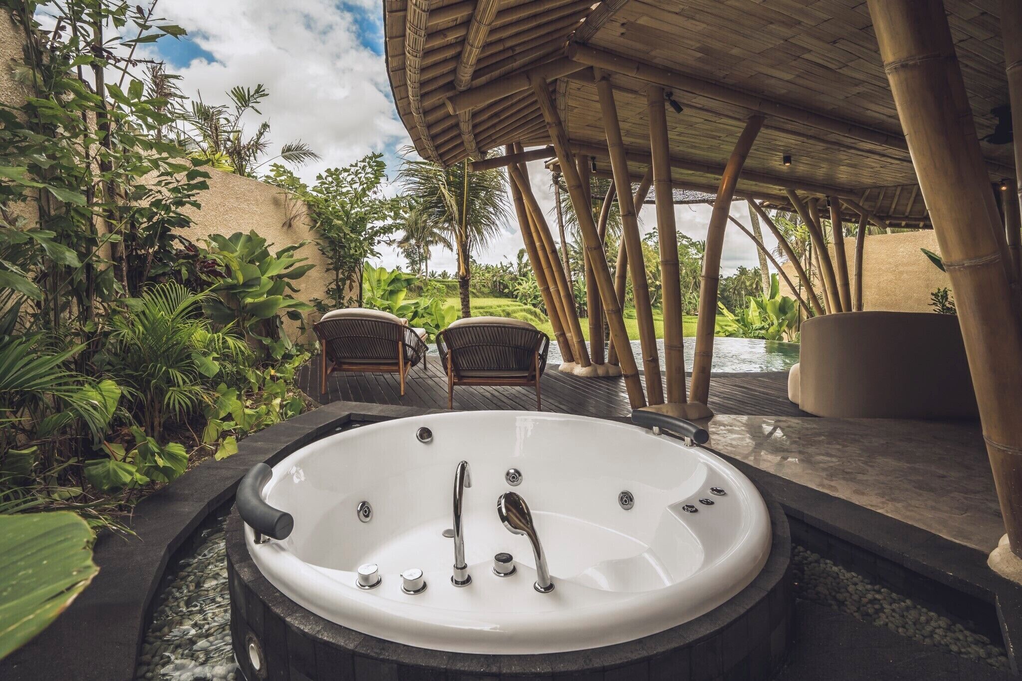 A hot tub surrounded by lush greenery, a covered seating area, and a pool.