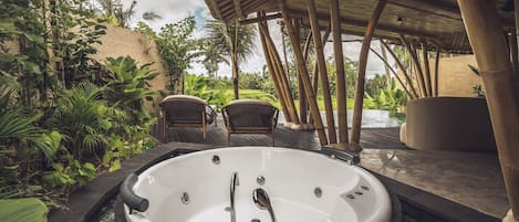 A hot tub surrounded by lush greenery, a covered seating area, and a pool.