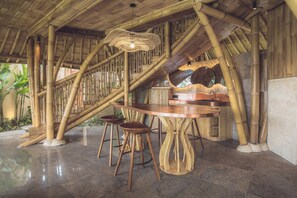 A bamboo-themed interior with a round table and stools, a hanging light fixture, and a curved wall. - Equipoise Resort Ubud by Ini Vie Hospitality (Tegallalang)