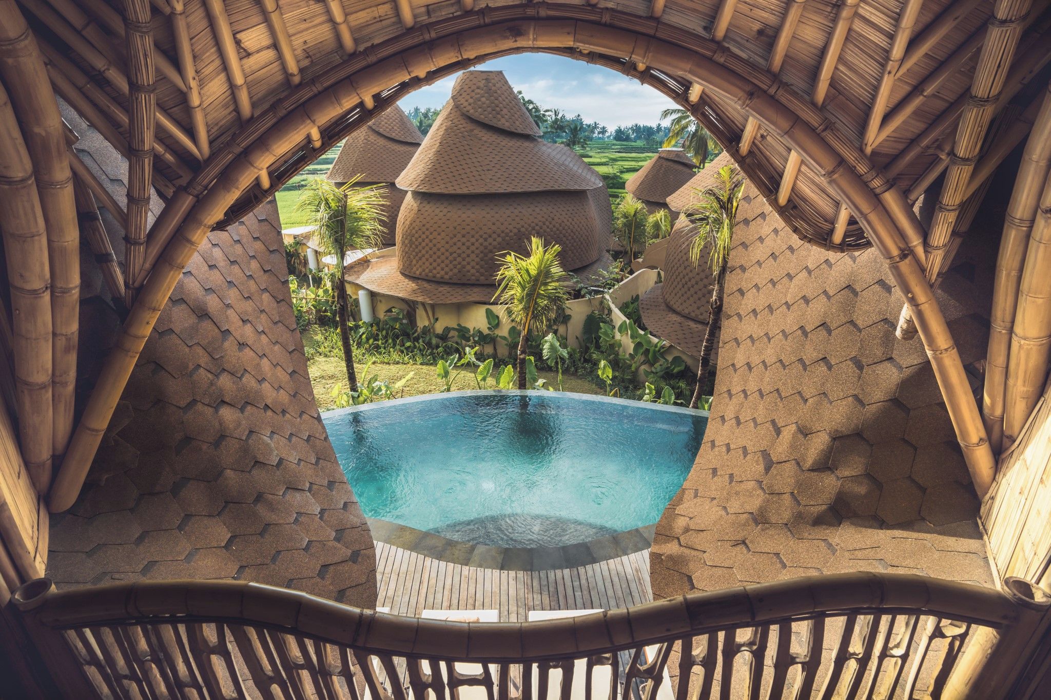 Zona de piscina con vista a una construcción tradicional de techo de paja y abundante vegetación.