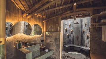 A rustic bathroom with a stone sink, a large mirror, and a stone shower enclosure.