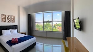 Une chambre d’hôtel avec un lit, une télévision, un bureau et une grande fenêtre donnant sur un beau paysage.