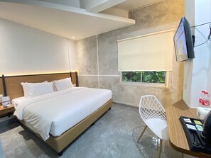 Camera d'albergo moderna con un letto, una scrivania con sedia, una TV e una finestra con vista sul verde.