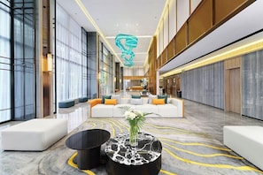 A spacious lobby with a central seating area, a modern chandelier, and a marble floor.