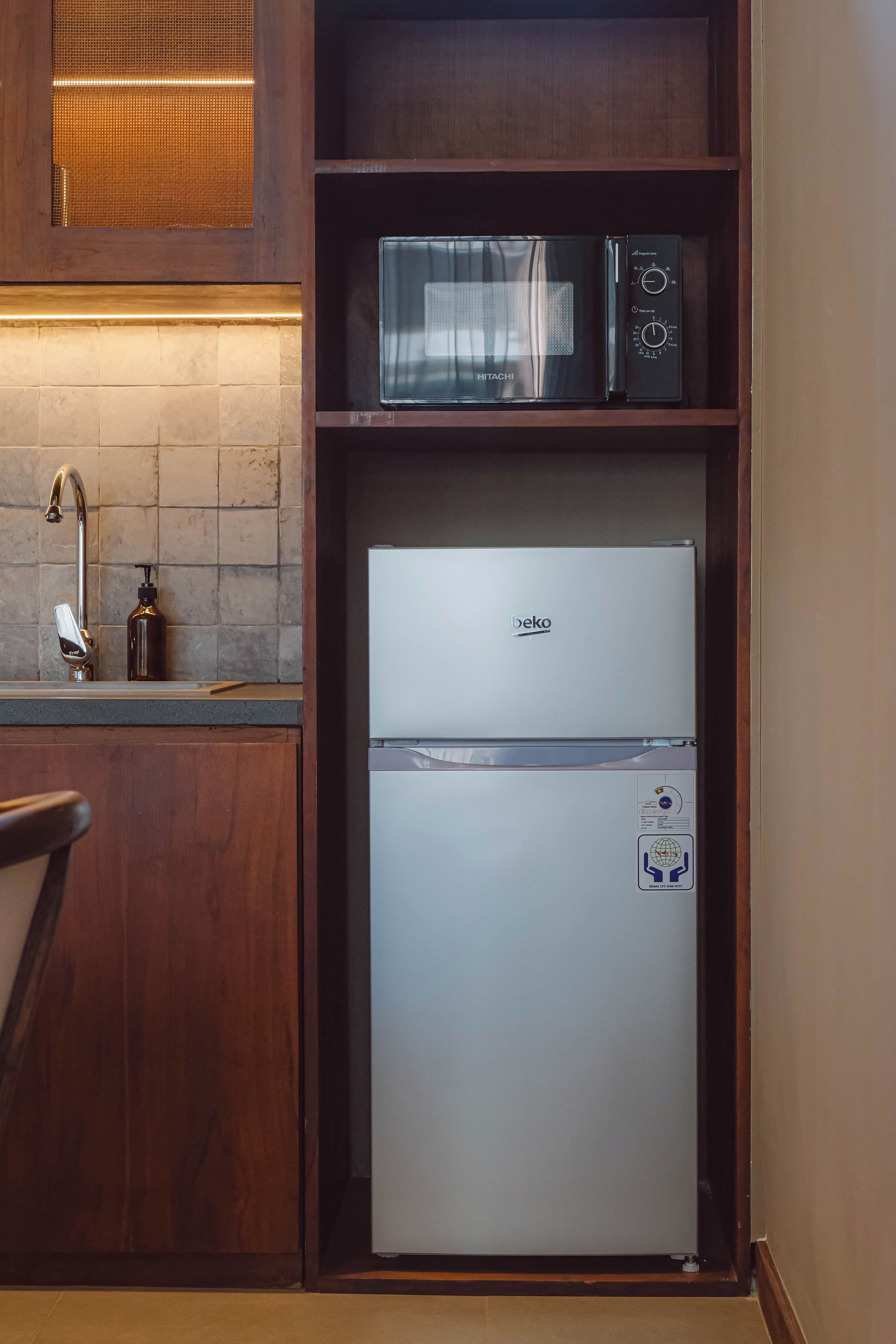 Una cocina compacta con microondas integrado, un refrigerador y un lavamanos con grifo.