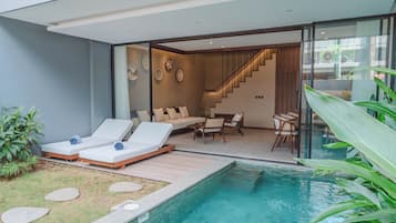Et moderne poolområde med liggestole, en trappe op til en etage og et spiseområde med stole og bord.
