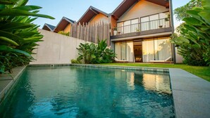 Una casa moderna de dos pisos con piscina, rodeada de exuberante vegetación.