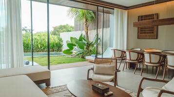 A modern living room with a large glass door leading to a pool, a dining area with chairs, and a large plant.