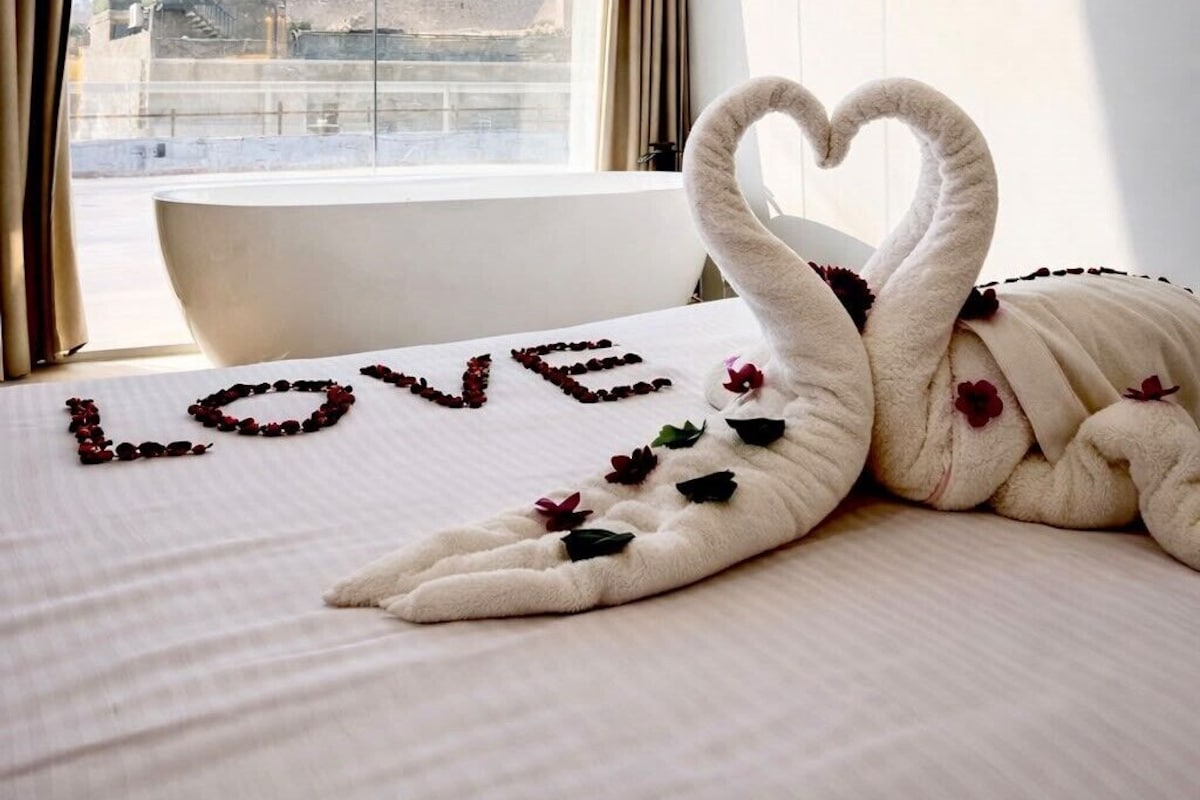 A hotel room with a bed, a heart-shaped towel arrangement, and a view of a pyramid.