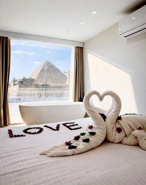 A hotel room with a bed, a heart-shaped towel arrangement, and a view of a pyramid. - Le Grand Pyramids View & Suites (Giza)