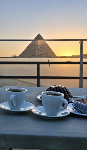 A table with two cups of coffee and a dessert, overlooking a pyramid and a body of water. - Le Grand Pyramids View & Suites (Giza)