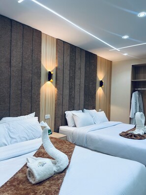 A hotel room with two beds, a wooden accent wall, wall-mounted lights, a robe, and a towel on the floor. - Le Grand Pyramids View & Suites (Giza)