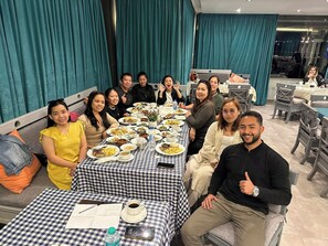 A group of people seated around a table with various dishes, in a room with teal curtains and a checkered tablecloth. - Le Grand Pyramids View & Suites (Giza)