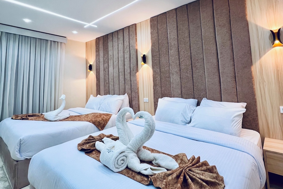 A hotel room with two beds, each with white linens and a swan-shaped towel arrangement.