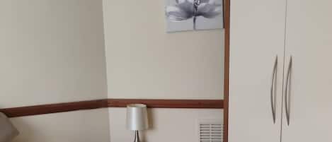 Un dormitorio con cama, mesita de noche, lámpara, armario y un cuadro colgado en la pared.