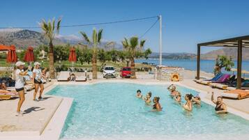 A swimming pool with people around it, a clear sky, and a mountainous landscape in the background.