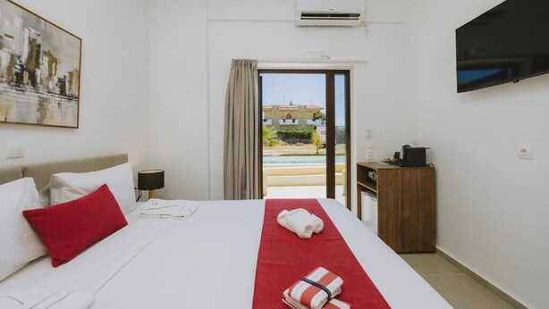 Une chambre d’hôtel équipée d’un lit, d’une télévision, d’un climatiseur, d’une fenêtre donnant sur une piscine et d’une table de chevet en bois.