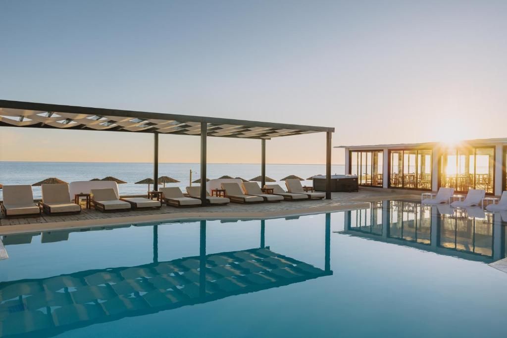 A pool area with lounge chairs and umbrellas, a covered seating area, and a view of the sea.