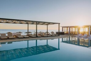 A pool area with lounge chairs and umbrellas, a covered seating area, and a view of the sea.