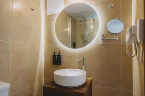 A bathroom with a round mirror, a sink, and a handheld hair dryer mounted on the wall. - Casa Di Notos Beach Hotel (Apokoronas)