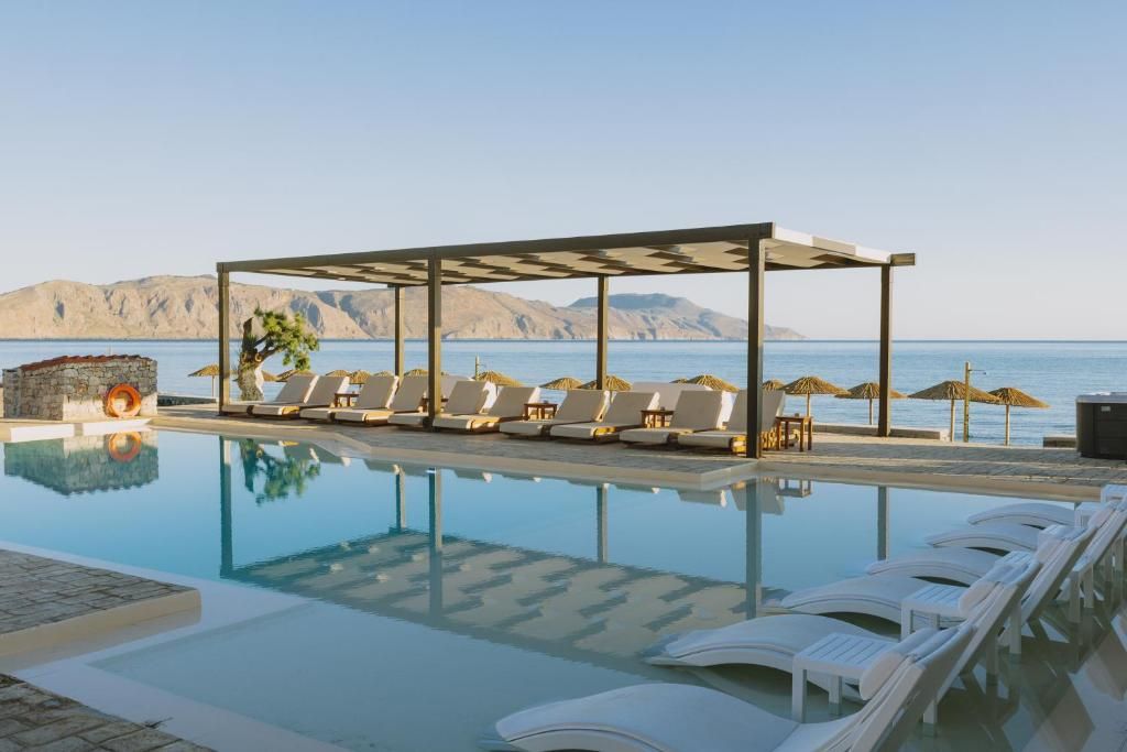 A pool area with lounge chairs and a pergola overlooking a body of water.