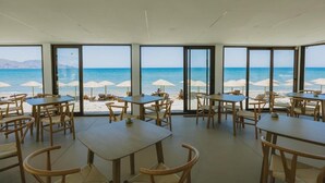 Un restaurant situé en bord de mer, avec des tables et des chaises, de grandes fenêtres et des parasols de plage.