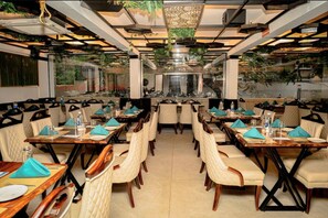 A restaurant with a modern interior, featuring a central dining area with long tables and chairs, surrounded by walls with large windows. - Citrus Classic Manyata Tech Park by Othpl (Bengaluru)