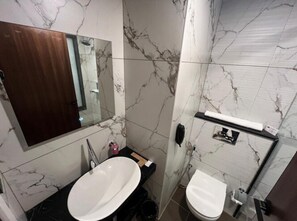 A bathroom with a marble wall, a sink, a toilet, and a mirror. - Citrus Classic Manyata Tech Park by Othpl (Bengaluru)