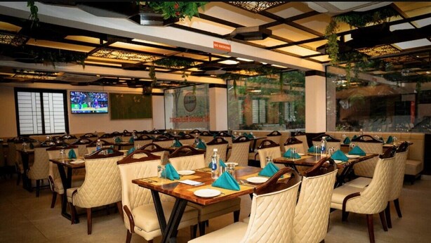 A restaurant with multiple tables and chairs, a television screen, and a sign indicating a smoking area. - Citrus Classic Manyata Tech Park by Othpl (Bengaluru)