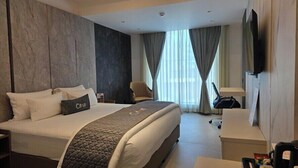A hotel room with a large bed, a desk, a chair, a television, and a window with curtains. - Citrus Classic Manyata Tech Park by Othpl (Bengaluru)