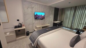 A modern hotel room with a large bed, a TV mounted on the wall, a desk, and a seating area. - Citrus Classic Manyata Tech Park by Othpl (Bengaluru)