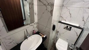 A bathroom with a marble wall, a sink, a toilet, and a mirror. - Citrus Classic Manyata Tech Park by Othpl (Bengaluru)
