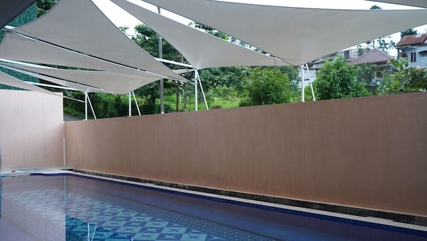 En pool med ett geometriskt mönster av kakel, omgiven av en låg mur och skuggad av vita markiser.