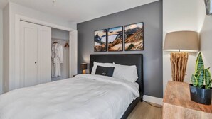 Un dormitorio con cama, mesita de noche, lámpara, planta y armario.
