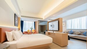 Ein modernes Hotelzimmer mit einem großen Bett, einem Fernseher und einer Sitzecke mit einer Couch und Sesseln.