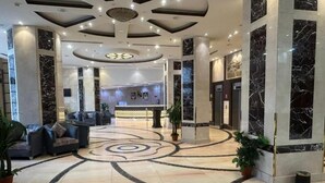 Vestíbulo de hotel con piso de mármol, zona de estar, mostrador de recepción y un diseño moderno de techo.