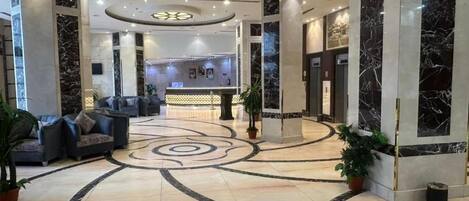 A hotel lobby with a marble floor, seating area, reception desk, and a modern ceiling design.